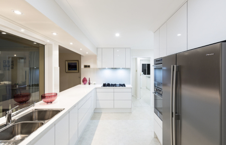 well lit white kitchen with wide windows and silver fridge