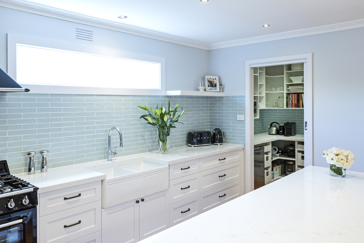 white kitchen with light blue tiles and wallpaper, door leading to extra storage